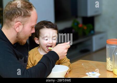 Young father feeding boy in home. Happy dad and son eating soup. Stock Photo