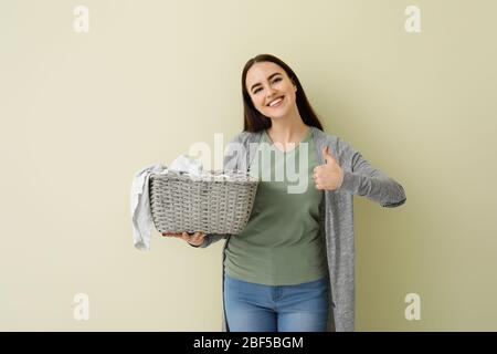 Beautiful young woman with laundry showing thumb-up on color background Stock Photo
