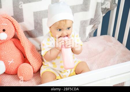 Cute baby drinking milk from bottle in crib Stock Photo