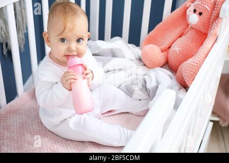 Cute baby drinking milk from bottle in crib Stock Photo
