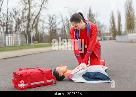 Paramedic demonstrating CPR on mannequin outdoors Stock Photo