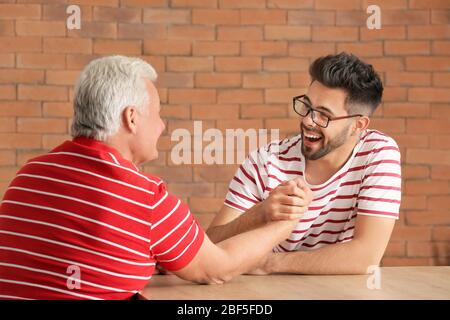 Young man and his father having arm-wrestling competition in kitchen Stock Photo