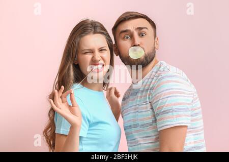 Funny young couple with chewing gums on color background Stock Photo