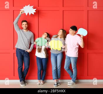 Group of young people with blank speech bubbles near color wall Stock Photo