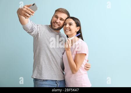 Happy young couple with pregnancy test taking selfie on color background Stock Photo