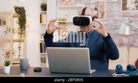 Retired man experiencing virtual reality using vr headset in living room. Cup of coffee on the table. Stock Photo