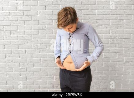 Overweight boy in tight clothes near brick wall Stock Photo