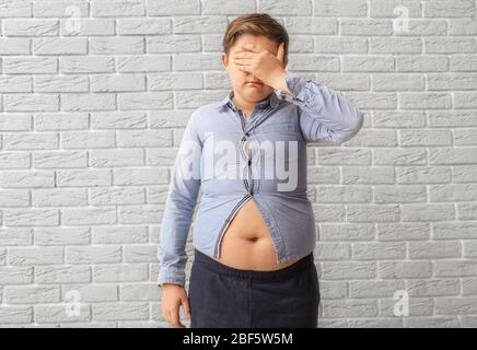 Sad overweight boy in tight clothes near brick wall Stock Photo