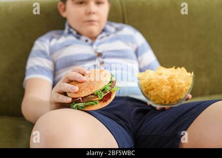 Overweight boy with junk food at home Stock Photo