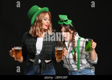 Funny young women with beer on dark background. St. Patrick's Day celebration Stock Photo