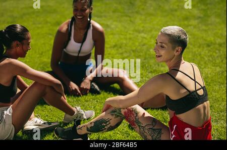 Group of three female soccer players relaxing on the field. Female soccer team players resting after training session in the ground. Stock Photo