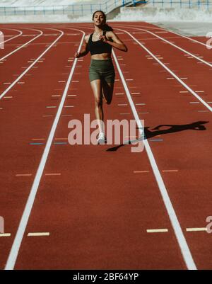 Female athlete sprinting on a running track in a track and field stadium. Woman runner training on a running track. Stock Photo