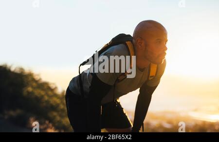 Man in sportswear taking break after trail run training. Male trail runner taking break, bending forward with hands on knees after running workout on Stock Photo