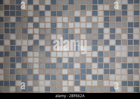 Close-up on a mosaic made of small gray, blue and white ceramic squares. It forms the floor of a lighted room Stock Photo