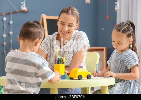 Nanny with cute little children playing and drawing at home Stock Photo