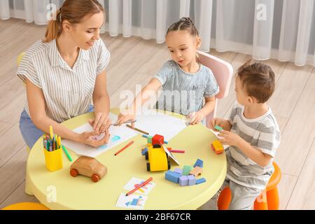 Nanny with cute little children playing and drawing at home Stock Photo