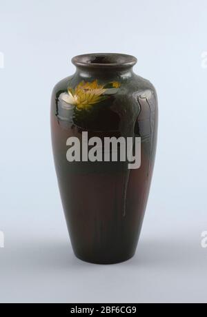 Vase. White clay body, thrown. Tall tapering baluster, incurving neck with turned out rim; no foot. Dark green lily pads arranged around body with yellow water lilies in various stages of bloom at the shoulder, all against a reddish-brown ground. Stock Photo