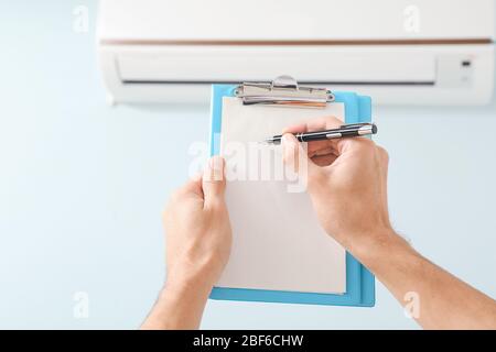 Male technician with clipboard checking operation of air conditioner indoors Stock Photo