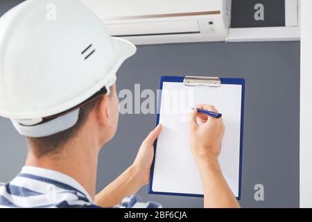 Male technician with clipboard checking operation of air conditioner indoors Stock Photo
