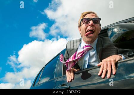 Excited businessman traveling in a car hanging out the window with wind blowing his tie and tongue Stock Photo