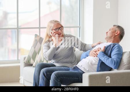 Mature woman calling an ambulance for her husband suffering from heart attack at home Stock Photo