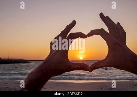 Male hands in the shape of a heart on the background of the sunset Stock Photo