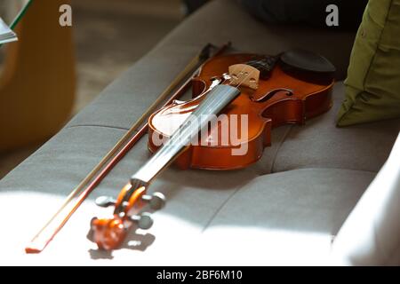 Close up shoot of violin lying on sofa in sunlight, hobby and music concept. Online courses or free information. Become musician, violinist while isolated, quarantine against coronavirus spreading. Using laptop, smartphone. Stock Photo