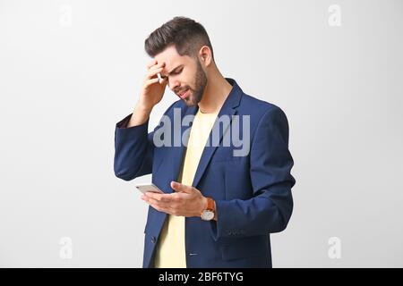 Worried young man with mobile phone on light background Stock Photo
