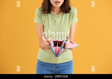 Young woman with empty wallet on color background Stock Photo