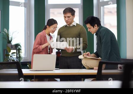Group of young people examining and discussing documents together they working in teamwork at office Stock Photo