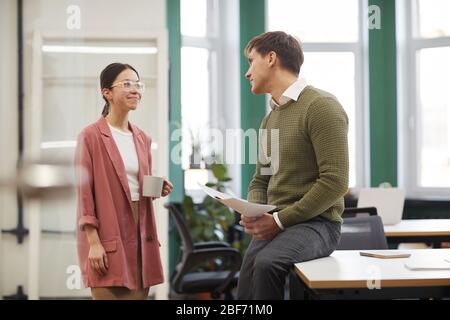 Young smiling businesswoman talking to her colleague and drinking coffee at office Stock Photo