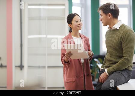 Young businesswoman in eyeglasses holding the contract and talking to businessman at office Stock Photo