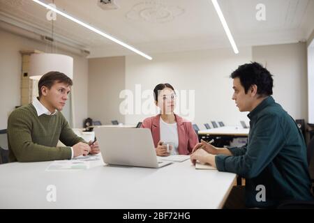 Group of business people sitting at the table in front of laptop and discussing new project at meeting Stock Photo