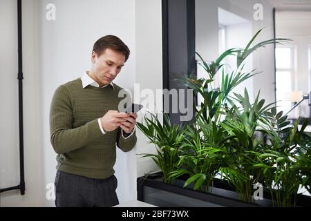 Young businessman using his mobile phone and texting a message while standing at office Stock Photo