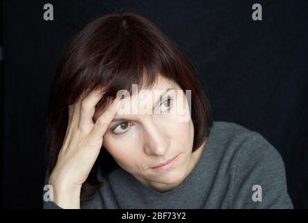 Mature, middle-aged woman looks anxiously away, touching forehead and hair with hand Stock Photo