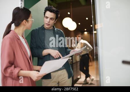 Young businessman discussing business documents together with young businesswoman while they standing at office Stock Photo