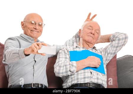 Elderly man taking photo with his sleeping friend on white background Stock Photo