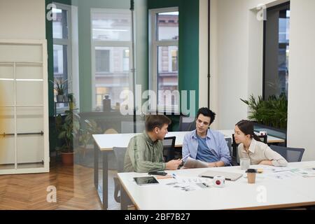 Team of designers sitting at the table and discussing new creative project together during meeting at modern office Stock Photo