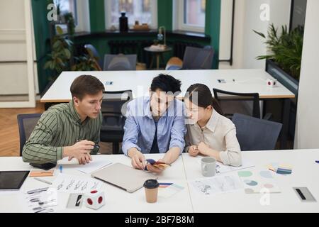 Group of creative designers examining colored patterns and working over new fashion collection at meeting at office Stock Photo
