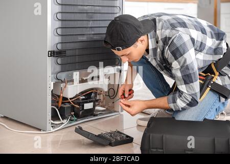 Worker repairing refrigerator in kitchen Stock Photo