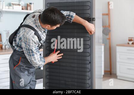 Worker repairing refrigerator in kitchen Stock Photo