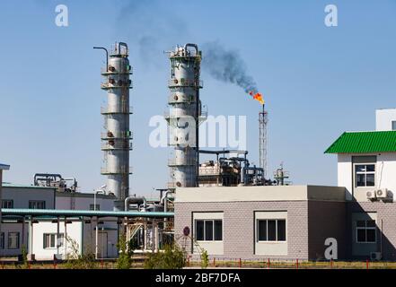 Distillation towers, burning gas torch, pipelines and industrial buildings on clear blue sky. Oil refinery and gas processing plant. Zhanazhol, KZ. Stock Photo
