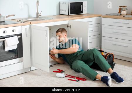 Handsome plumber repairing sink in kitchen Stock Photo
