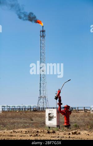Oil refinery plant. Fire extinguisher and tall gas torch mast on blue sky background. Stock Photo