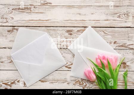 Envelopes with card and flowers on white wooden background Stock Photo