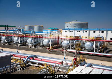 Panorama of oil refinery plant in desert. Pipelines, factory building, heat exchangers, oil storage tanks. Worker in white hardhat and red work wear. Stock Photo