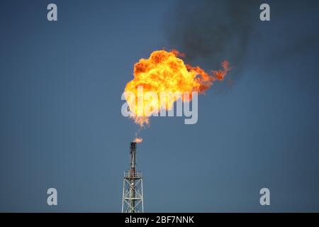 Burning orange nature gas torch. Strong flame. On oil refinery plant on deep blue sky. Stock Photo