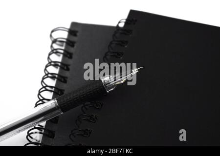One black colored ball point pen placed on top of two black color note diary on a white background Stock Photo