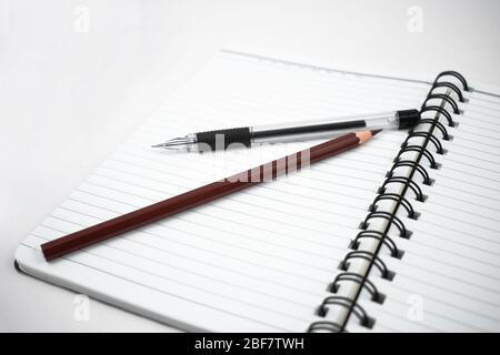 Pencil of brown color and a black color pen placed on top of a open white diary Stock Photo