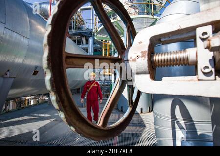Aktobe region/Kazakhstan - May 04 2012: Oil refinery plant. Asian refinery worker and steering wheel or valve. On refinery column and tank background. Stock Photo